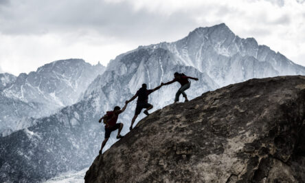 Three friends out rock climbing, helping each other in a dramatic setting