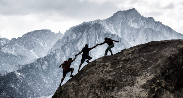 Three friends out rock climbing, helping each other in a dramatic setting